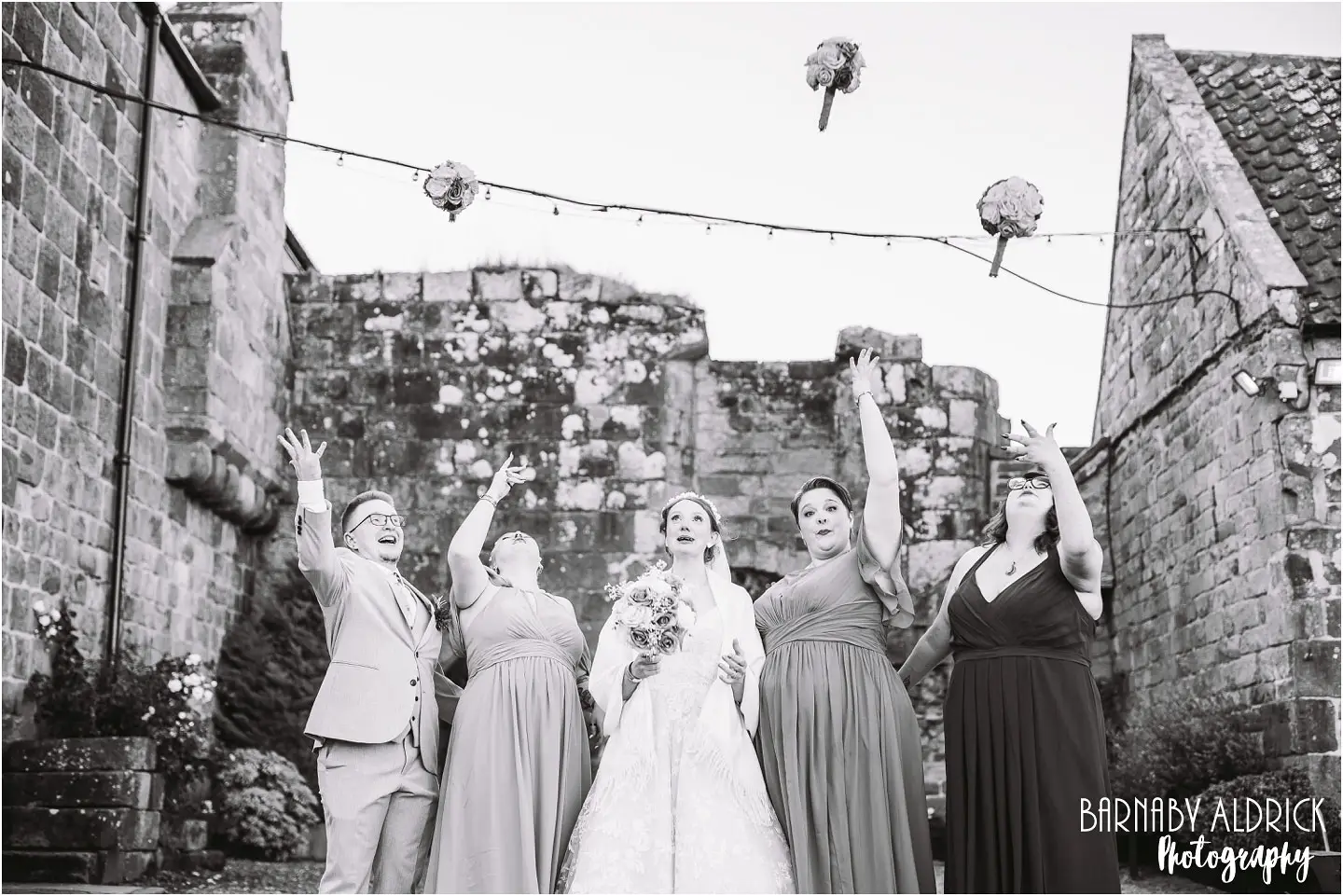 Fun wedding photo of bridesmaids tossing bouquets at Danby Castle Barns in Yorkshire