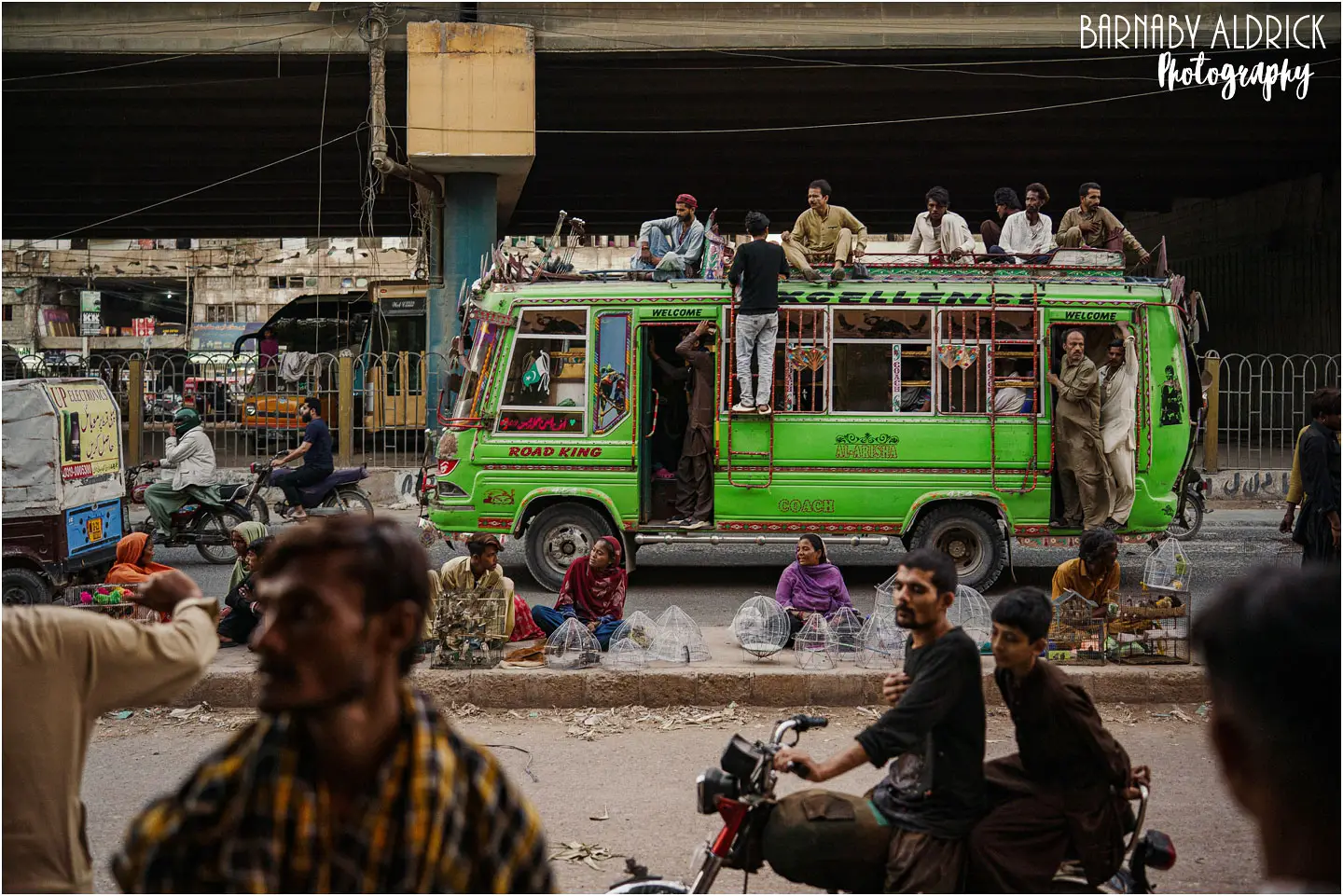 Karachi street photography green bus with people riding on the roof 2026
